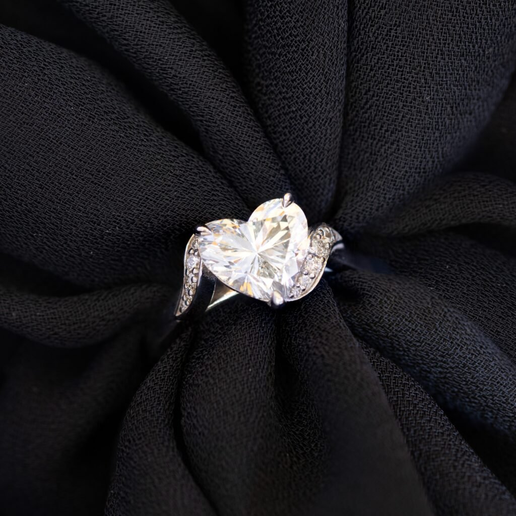Tina solitaire with heart cut diamond and diamond side stones on a black background.