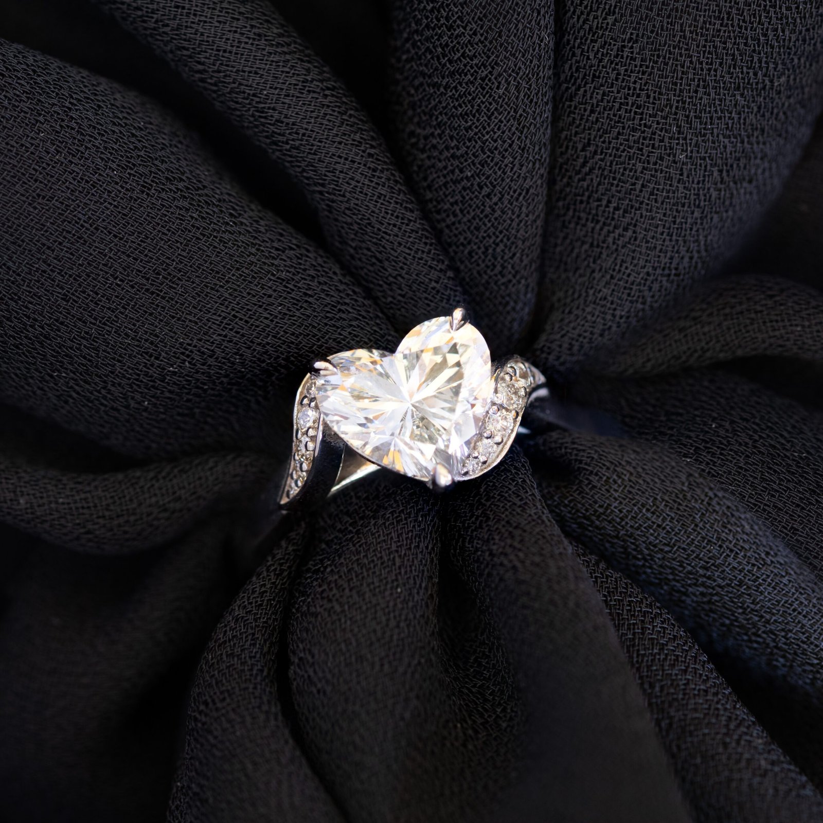 Tina solitaire with heart cut diamond and diamond side stones on a black background.